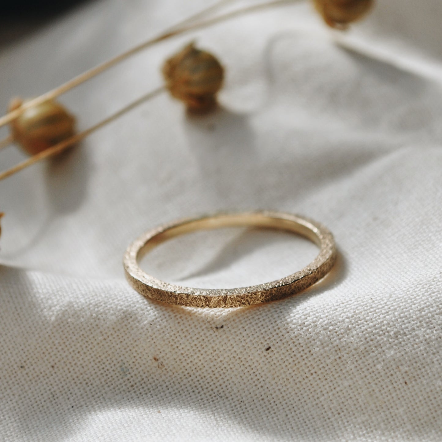 Square section ring, richly textured, laying on sunlit natural linen