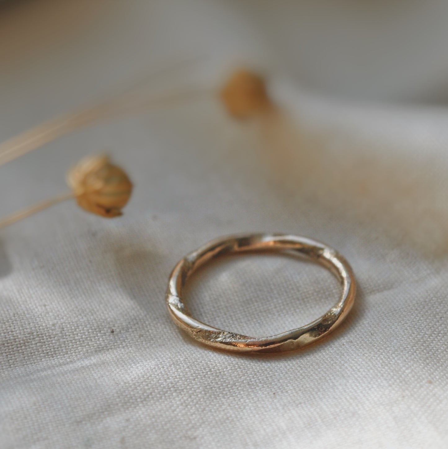 A handmade gold wedding band with textured twist detail, laying on soft natural linen